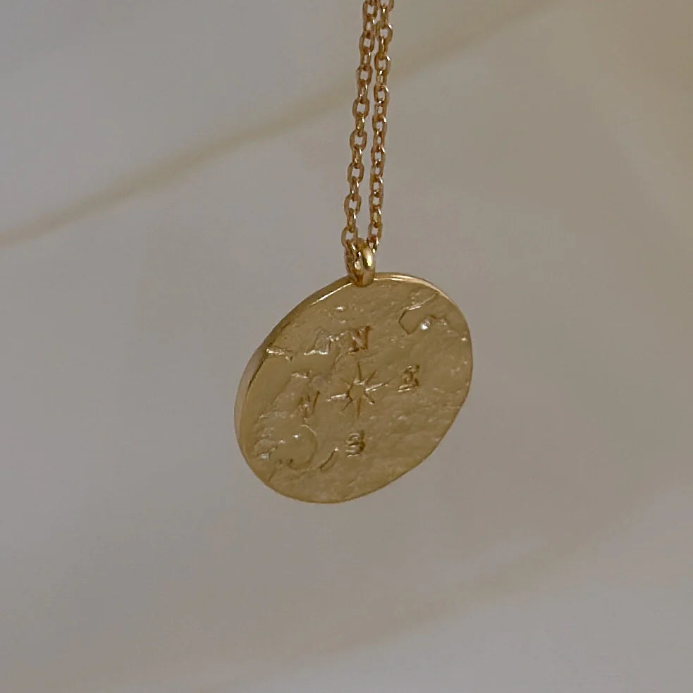 Zoom sur pendentif doré gravé d'une boussole sur fond clair. Collier atlas love local jewelry. Koolkado.